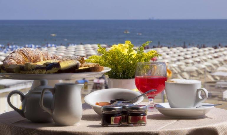 Colazione estiva al mare: caffè, dolci, fiori, e vista sulle onde.