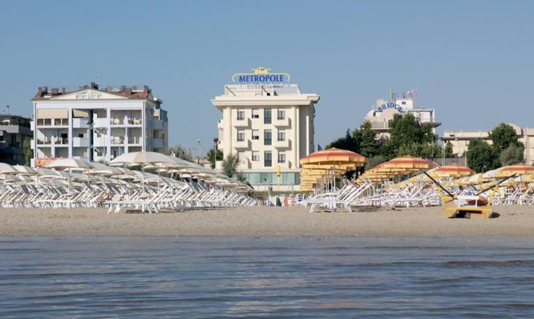 Spiaggia soleggiata con ombrelloni colorati, hotel Metropole sullo sfondo.